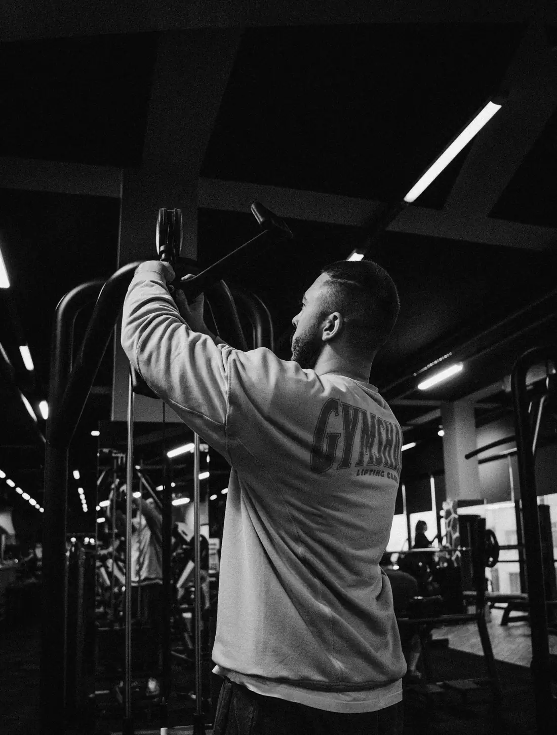 Atleta di spalle che esegue una trazione alla lat machine in una sala pesi in penombra