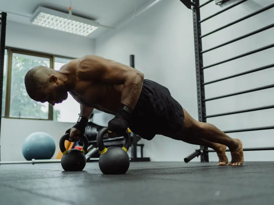 Uomo che esegue piegamenti appoggiandosi a due kettlebell sul pavimento della sala